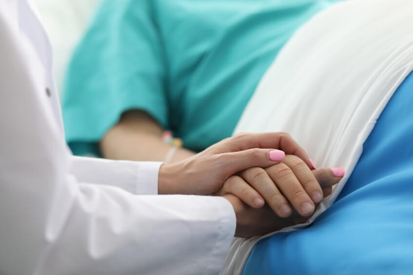 doctor holding patient’s hand with serious condition in hospital bed